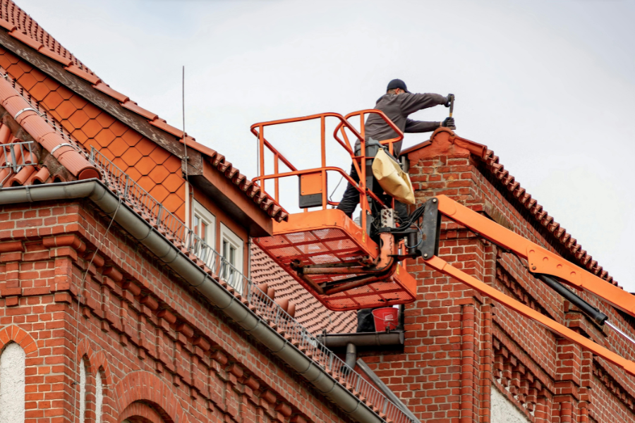 Worker inspecting and repairing red shingle roof